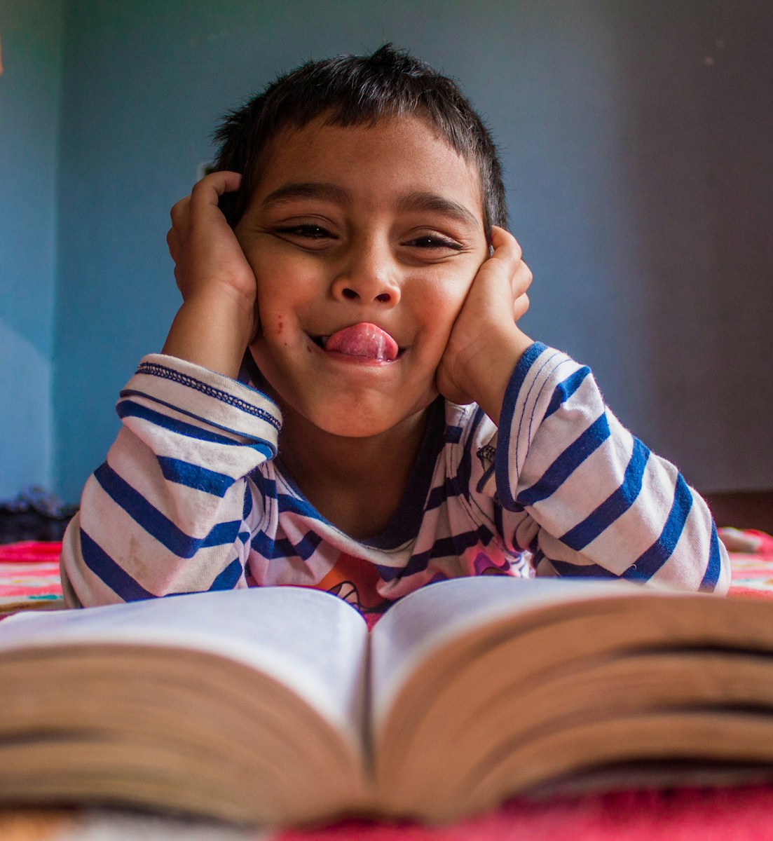Young boy sticking tongue out at book