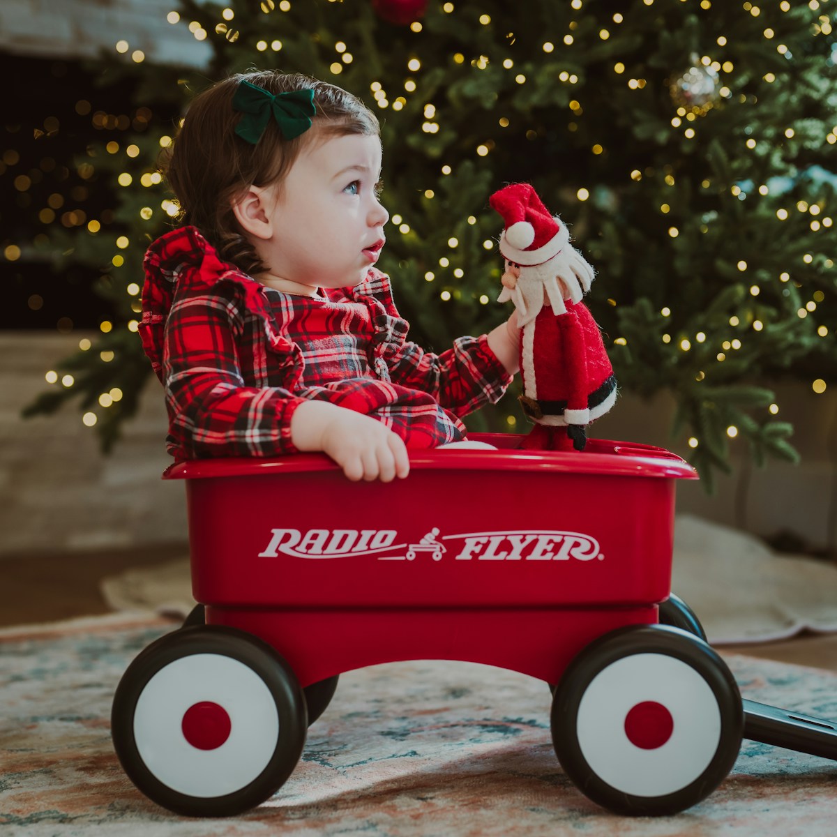Baby in red wagon with santa toy near christmas tree